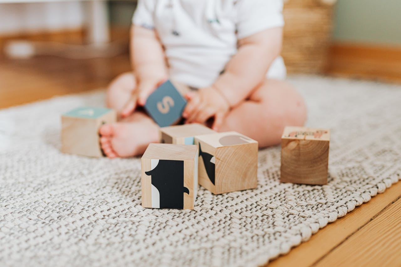 A baby engaging in play with wooden blocks on a textured carpet indoors.